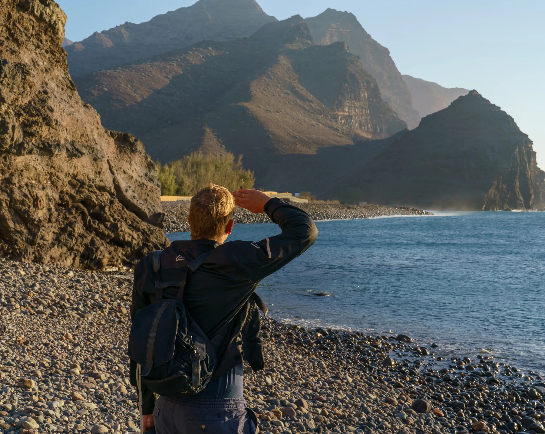 Person ser ut over dramatiske fjell fra steinstranden